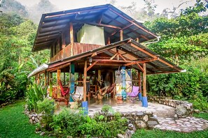 Uma casa de madeira rústica com telhado inclinado, rodeada por vegetação exuberante.