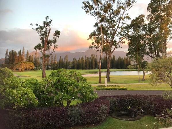 Um campo de golfe com um lago, árvores e montanhas ao fundo.