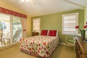 Quarto com colcha florida, parede verde e vista do exterior por uma porta de correr de vidro.