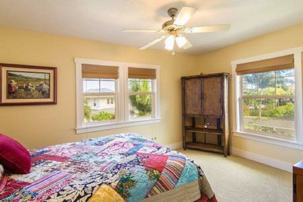 A bedroom with a bed, a ceiling fan, a window with blinds, a wooden cabinet, and a framed picture on the wall.