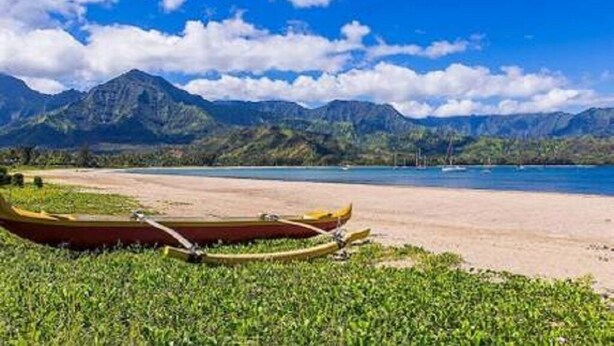 Una playa con montañas al fondo y una canoa en la arena.