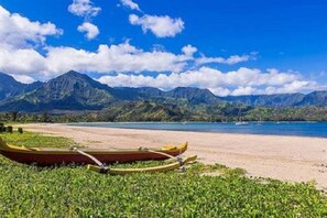 A beach with mountains in the background and a canoe on the sand. - NO 17.96% TAXES. Relax & Enjoy 3-3 Unobstructed Mountain Views. Pool Gym.  (Princeville)