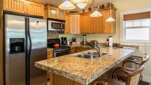 Una cocina con armarios de madera, electrodomésticos de acero inoxidable, encimeras de granito e iluminación colgante.