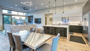 Een moderne keuken met een centraal eiland, barstoelen en een eethoek met een grote tafel en stoelen.