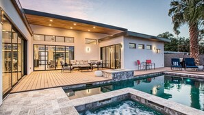 Een modern huis met een zwembad, een houten terras en een zitgedeelte buiten.