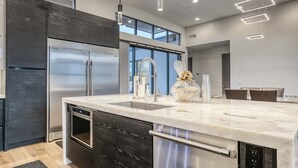 Een moderne keuken met een groot eiland, roestvrijstalen apparatuur en een hoge plafond met inbouwverlichting.