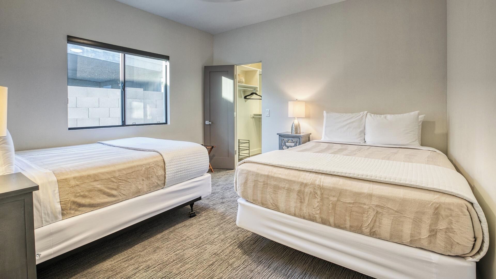 Habitación de hotel con dos camas individuales, ventana, puerta que da al baño y una mesita con lámpara.