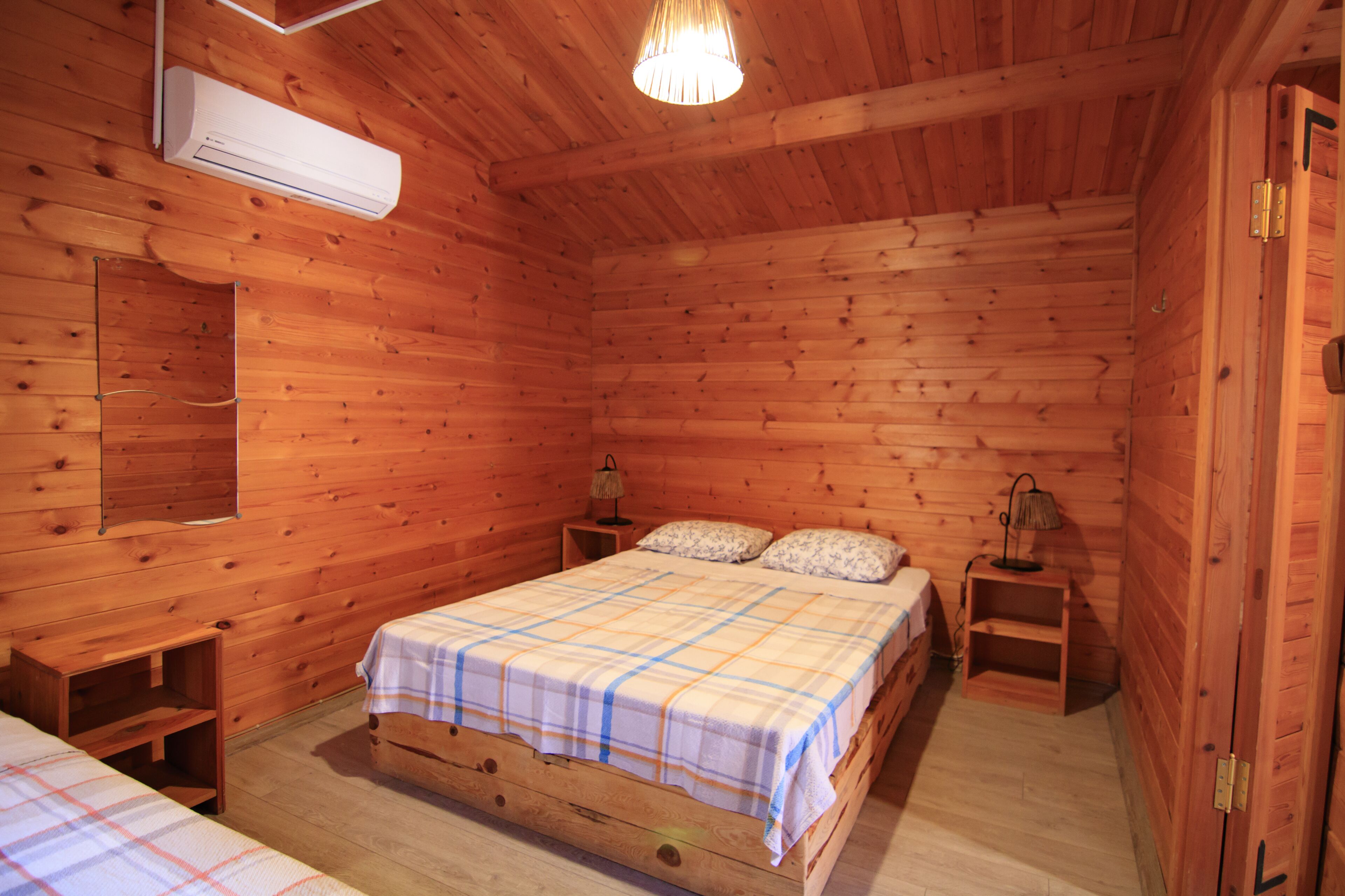 Ein Zimmer in einer Holzhütte mit einem Bett, Nachttischen, einer Lampe und einer Klimaanlage.