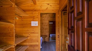 A wooden cabin interior with a wooden door, a bed, and a small table. - Agora Sanat Köyü (Ezine)