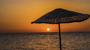 A beach umbrella with a woven design, positioned against a sunset over the ocean. - Agora Sanat Köyü (Ezine)