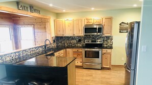 A modern kitchen with granite countertops, stainless steel appliances, wooden cabinets, and a large island with bar stools. - Lakeside Paradise on Berlin  (Deerfield)