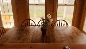 A wooden dining table with four chairs, a potted plant, and large windows offering a view of a fenced yard and a body of water. - Lakeside Paradise on Berlin  (Deerfield)