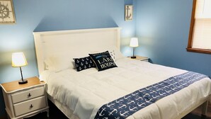 A neatly made bed with a white headboard and a navy blue blanket with anchor patterns. There are two nightstands with lamps and a small drawer on the left. - Lakeside Paradise on Berlin  (Deerfield)