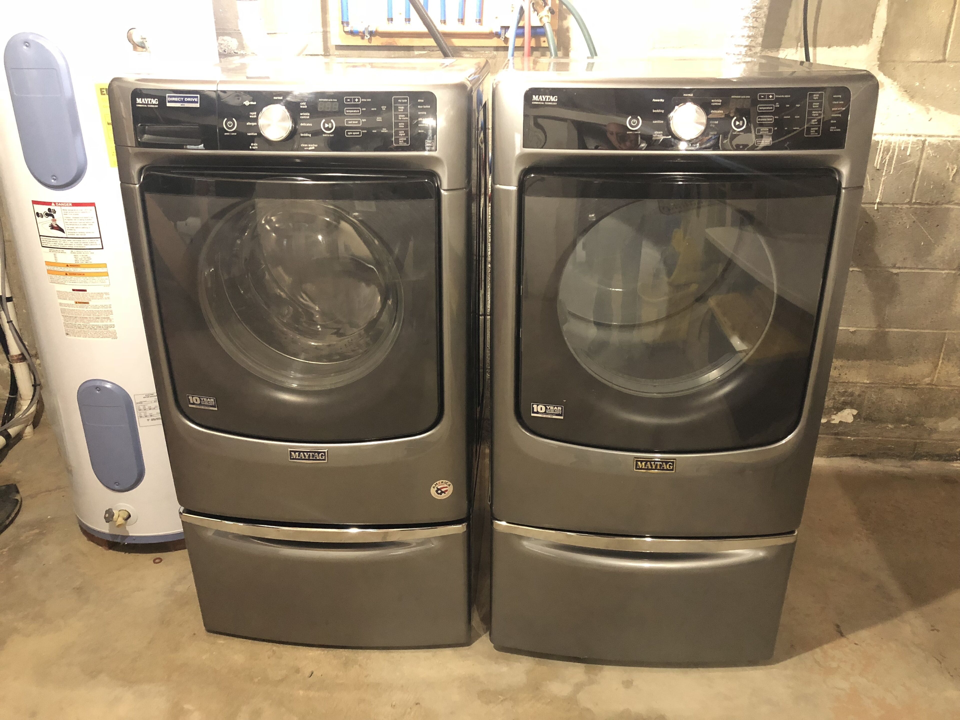 Two Maytag front-loading washing machines with control panels, placed next to a white appliance with a blue handle.