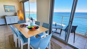 A dining area with a table, chairs, and a fruit bowl. There is a view of the ocean through large windows. - Breathtaking Ocean Views - 2 bedroom apartment with parking (Tamarama)