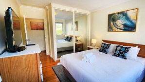 A hotel room with a bed, a TV, a desk, and a bathroom. - Breathtaking Ocean Views - 2 bedroom apartment with parking (Tamarama)