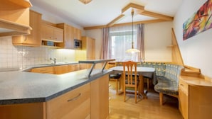 A compact kitchen with wooden cabinets, a built-in microwave, and a dining area with a table and chairs.