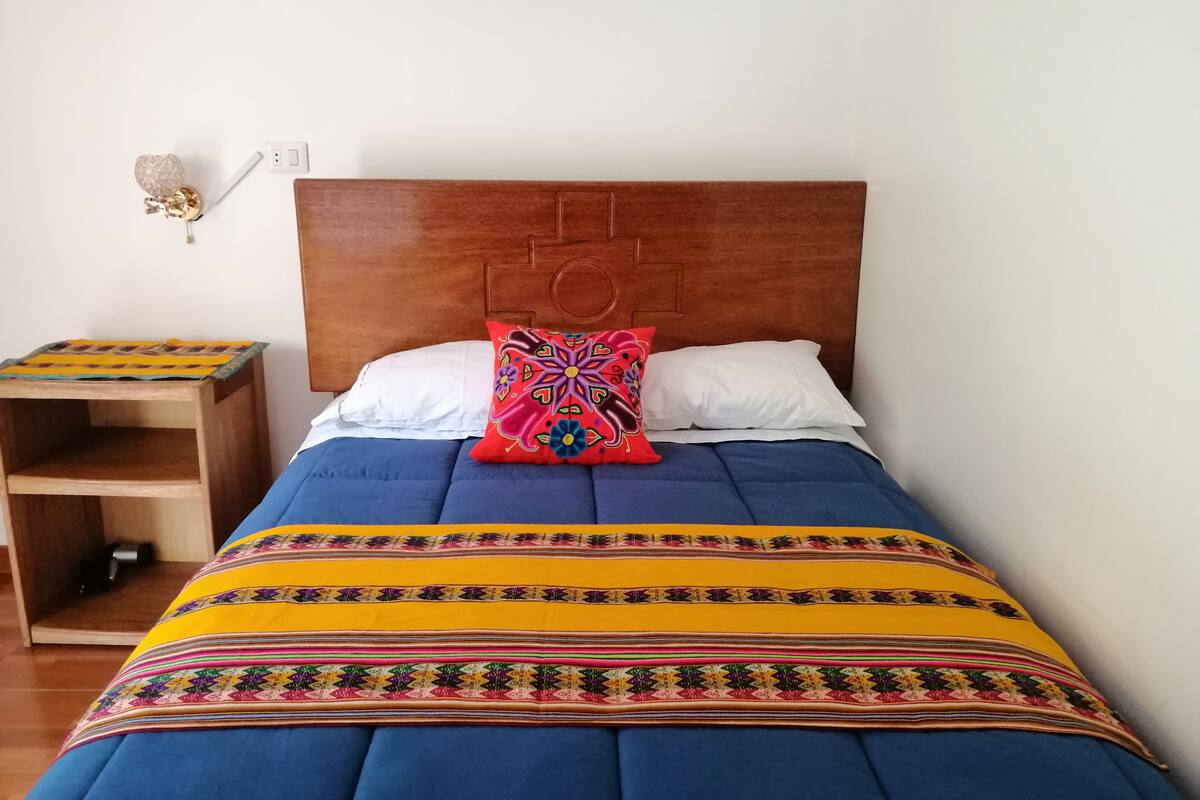 A bed with a wooden headboard, a colorful blanket, and a small wooden nightstand with a lamp.