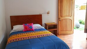 Una cama con colcha azul y almohada rosa, una mesita de noche de madera y una puerta de madera.