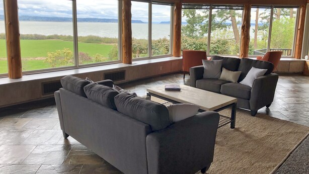 A spacious room with large windows offering a view of a lake and greenery. There are two sofas and a coffee table. - The Alpaca Retreat - Luxury farm house with water view! (Camano Island)