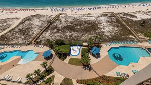 Vista aérea de un complejo turístico en la playa, con varias piscinas, tumbonas y una zona de arena.