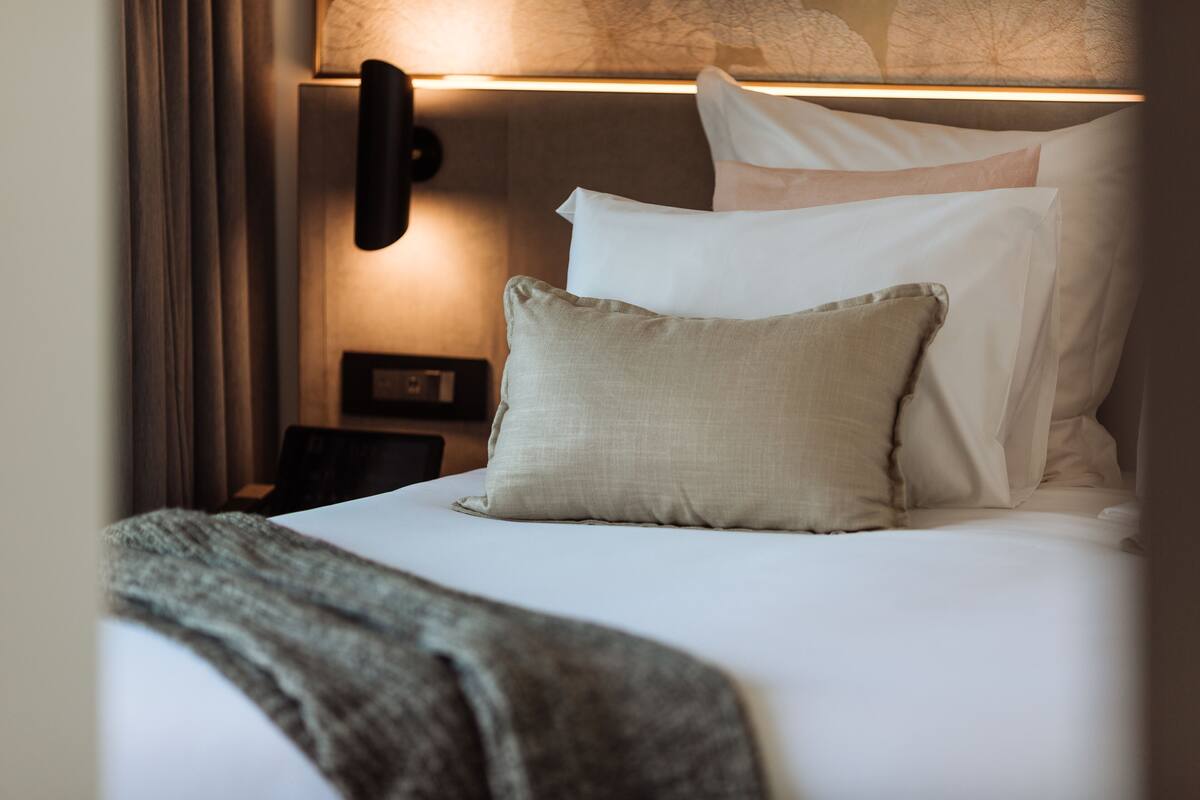 Un lit bien fait, avec du linge de lit blanc et un plaid beige.