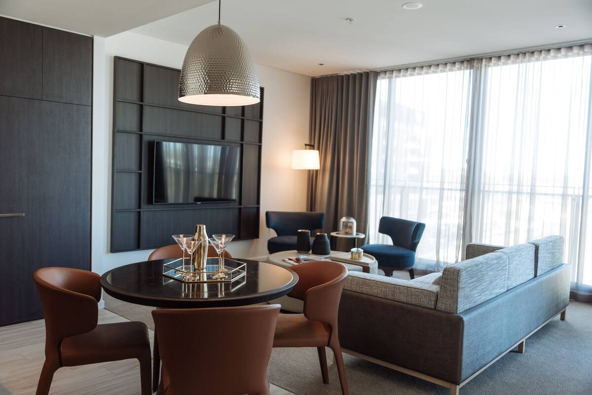 Un salon moderne avec une table à manger ronde, des chaises marron, un canapé gris et un téléviseur fixé au mur.