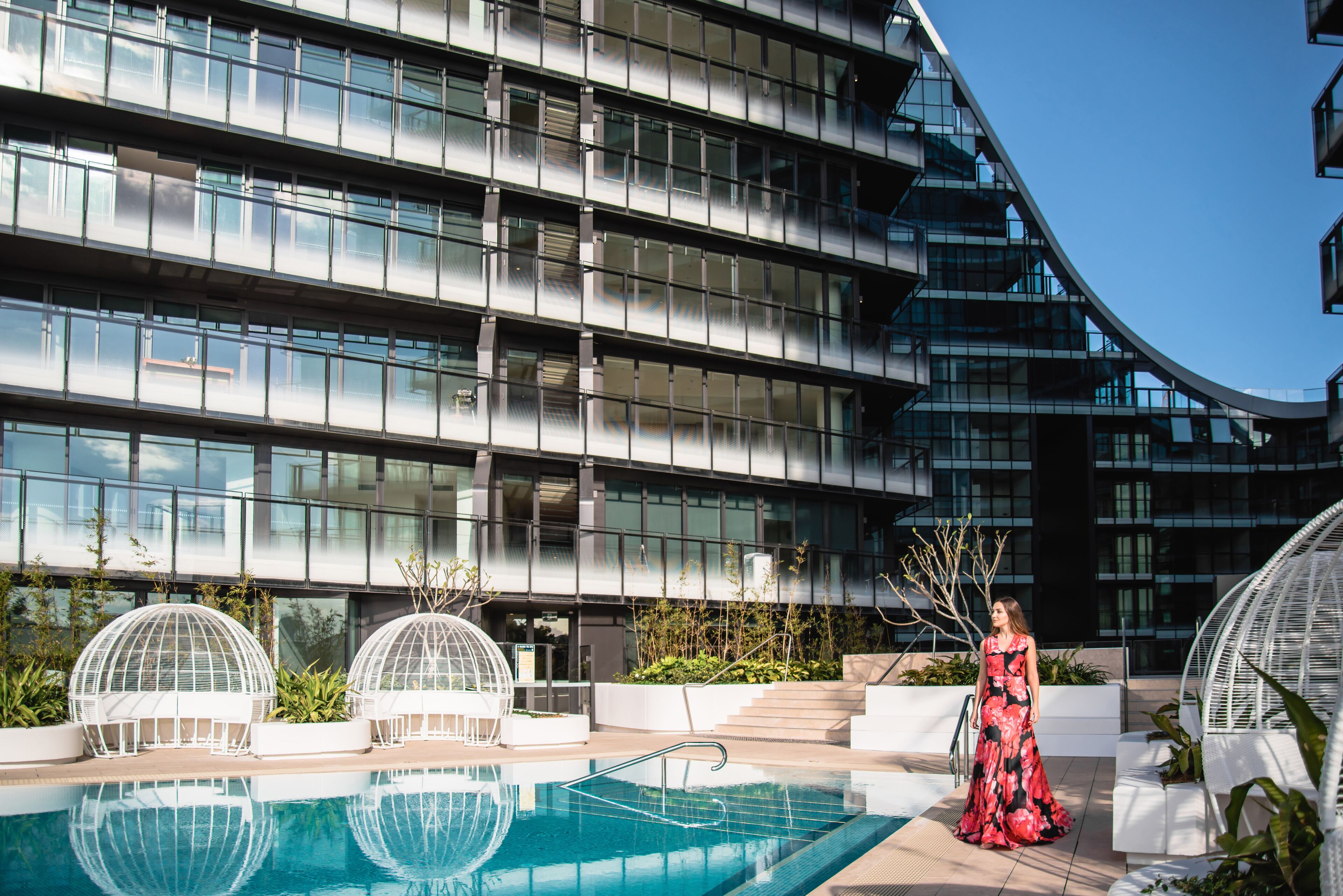 A modern building with a pool, white spherical structures, and a woman in a dress.