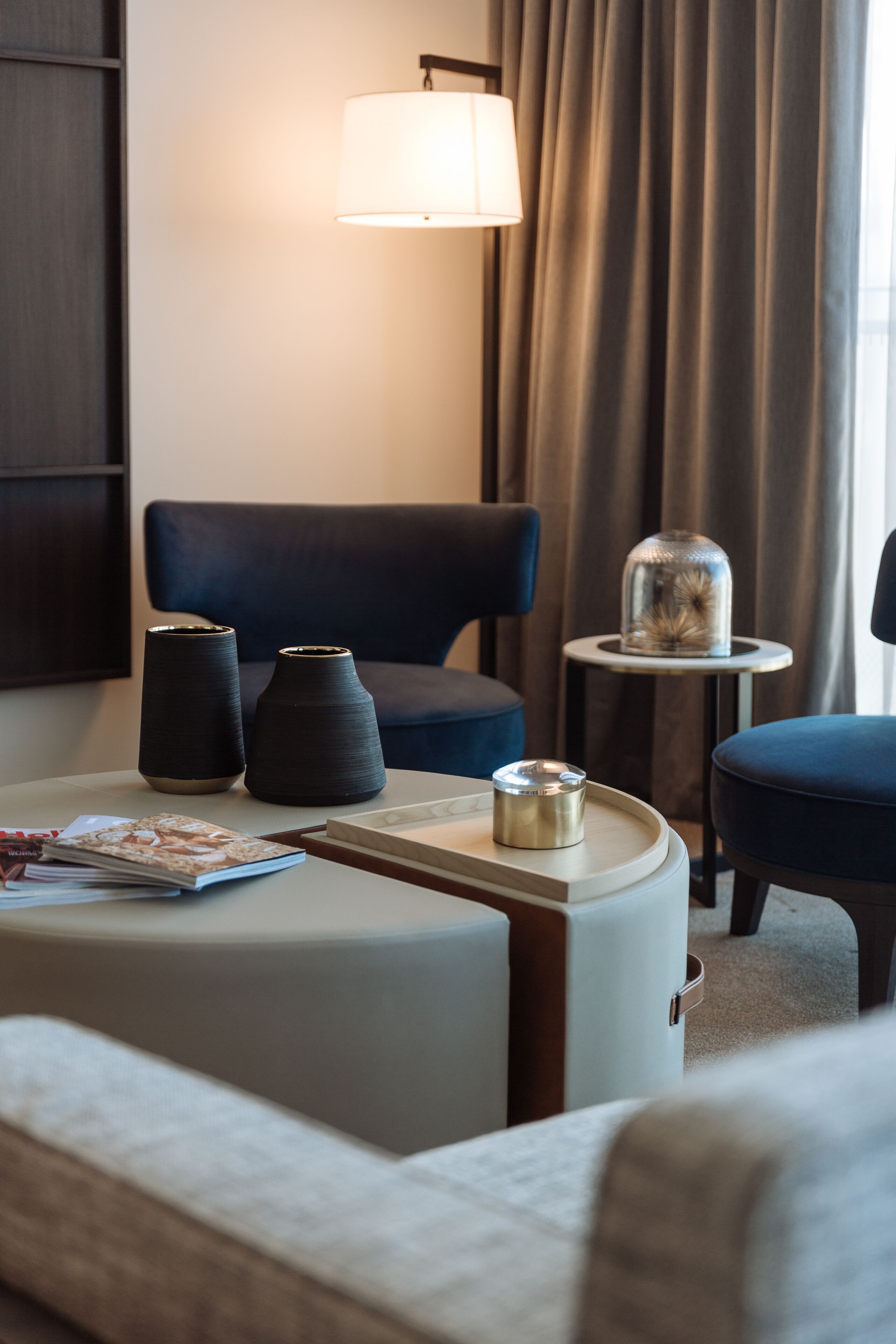A hotel room with a modern design, featuring a sofa, a small table with a lamp, and two decorative vases.