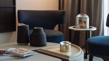 A hotel room with a modern design, featuring a sofa, a small table with a lamp, and two decorative vases.