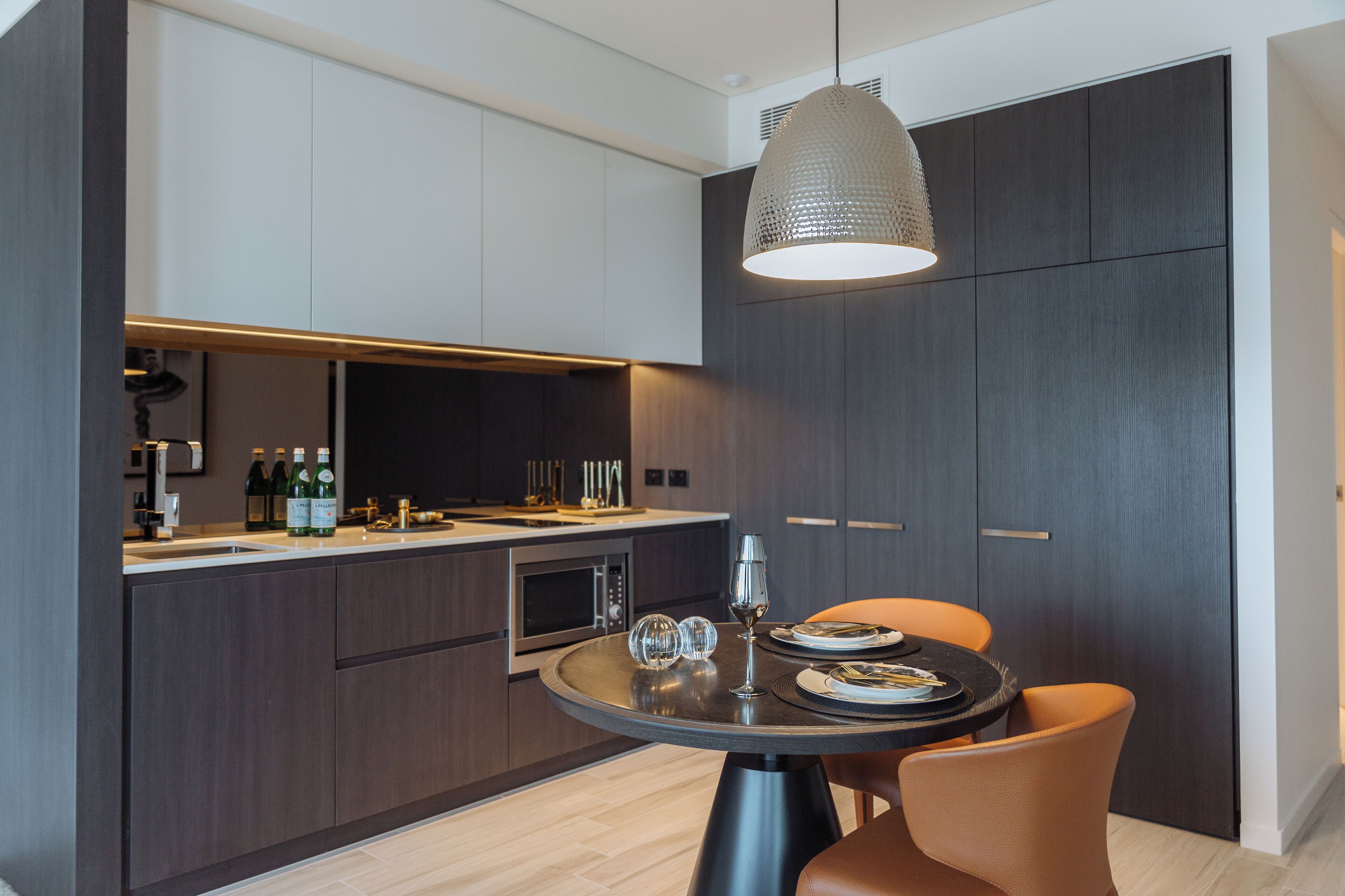A modern kitchen with dark cabinetry, a round dining table, and orange chairs.
