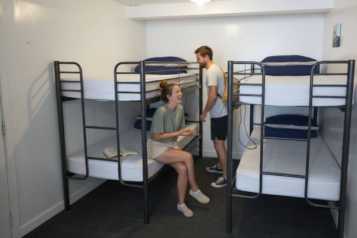 Une chambre de dortoir avec des lits superposés, une porte blanche et un interrupteur sur le mur.