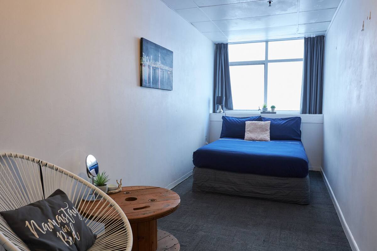 Une chambre à coucher avec un lit, une chaise, une petite table et une fenêtre avec des rideaux.