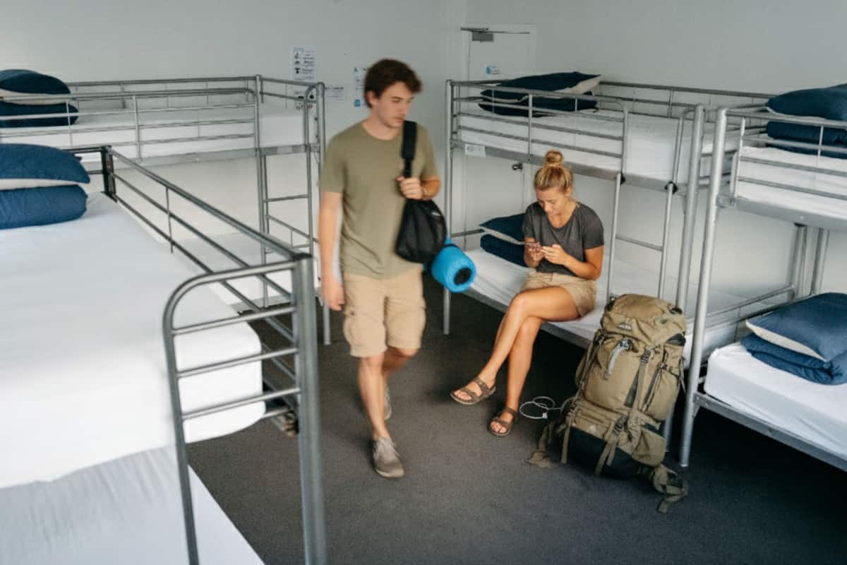 Une chambre de dortoir avec des lits superposés, un tapis de yoga bleu et un sac à dos posé sur le sol.