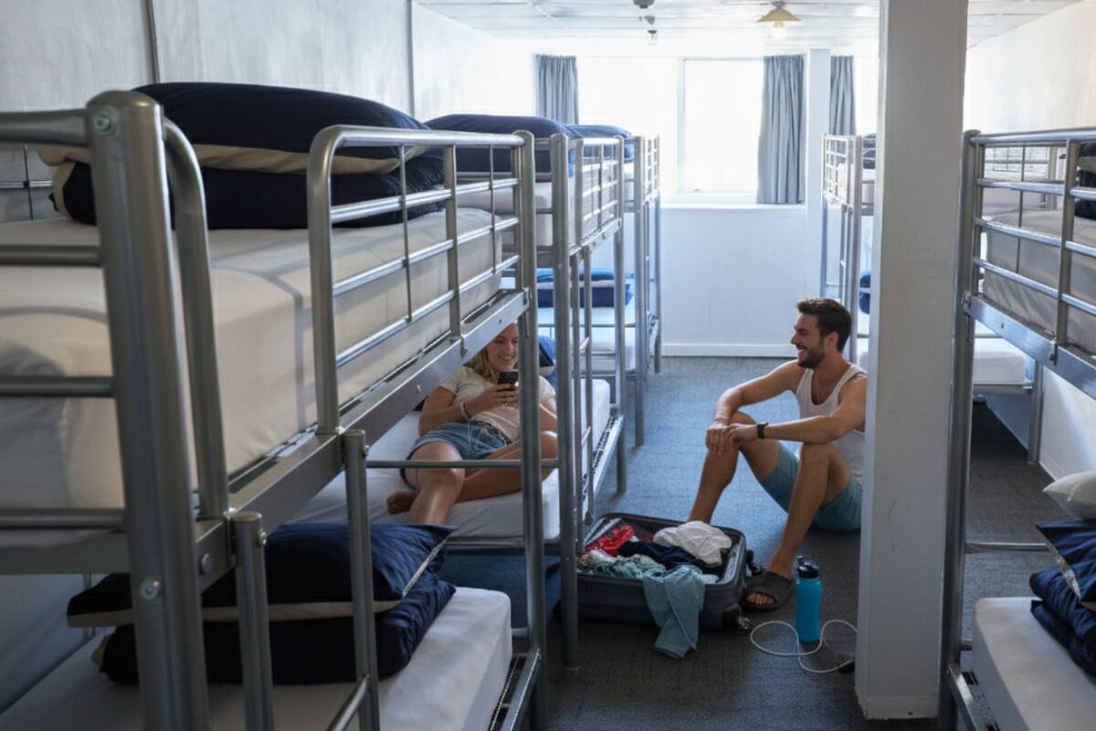 Une chambre de dortoir avec des lits superposés, une petite table et une valise posée sur le sol.