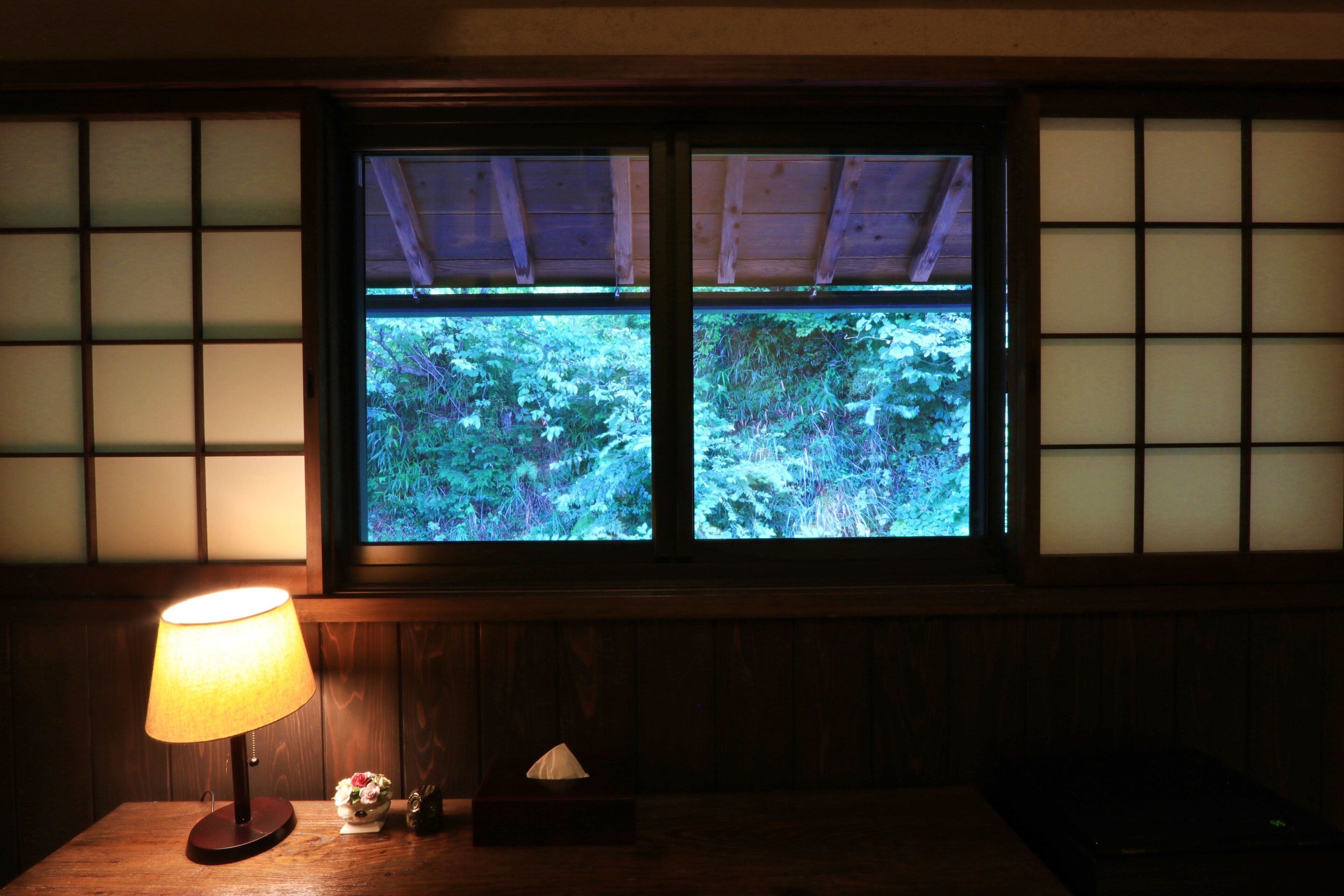 Una habitación con una mesa de madera, una lámpara y una ventana que da a zonas verdes.