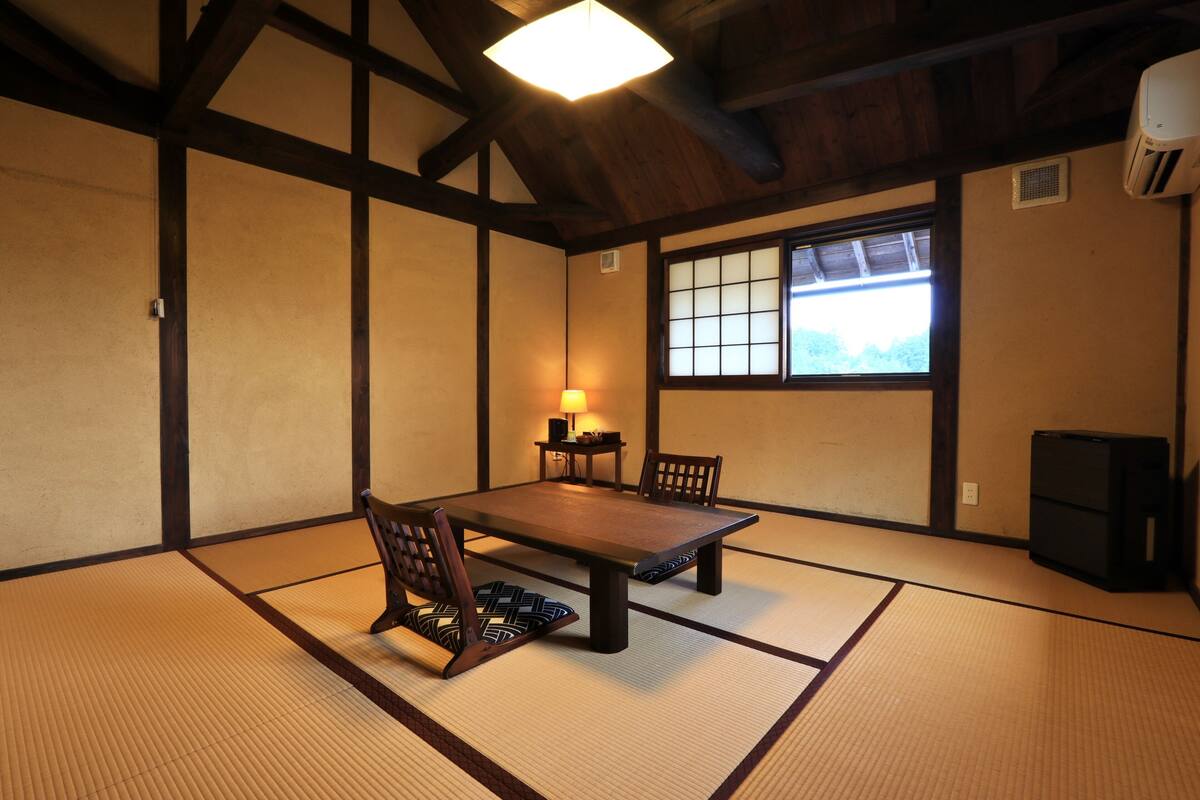 A tatami mat room with a low table and chairs, a window with a view, and a ceiling fan.