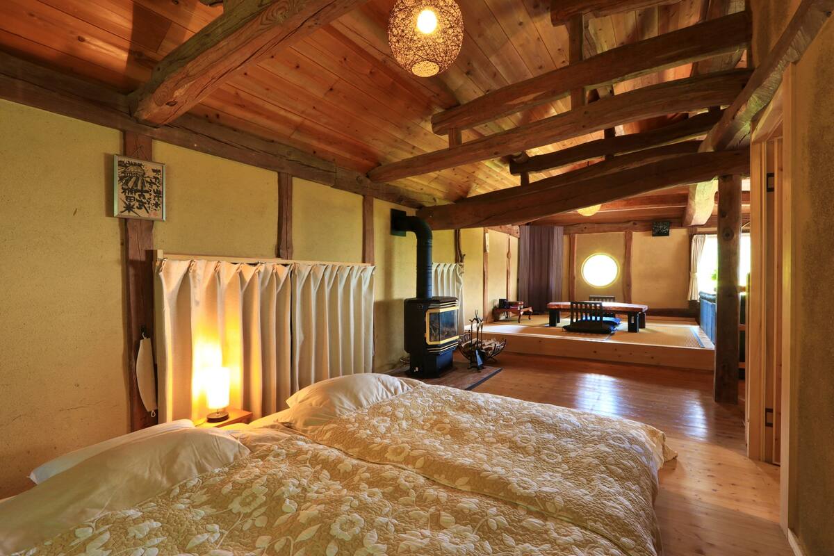A cozy room with a large bed, a wooden ceiling, a wall-mounted heater, and a small table with chairs.