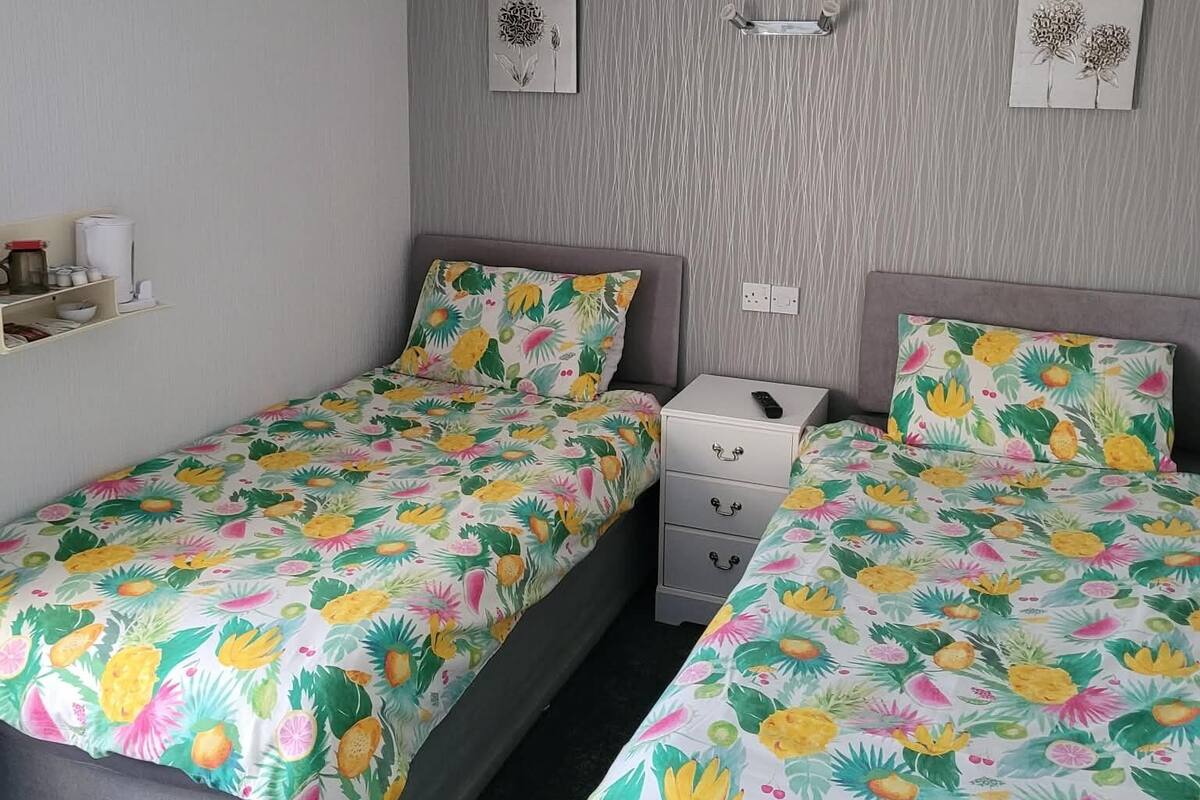 Un dormitorio con dos camas, una mesita de noche, un estante en la pared y un respiradero.