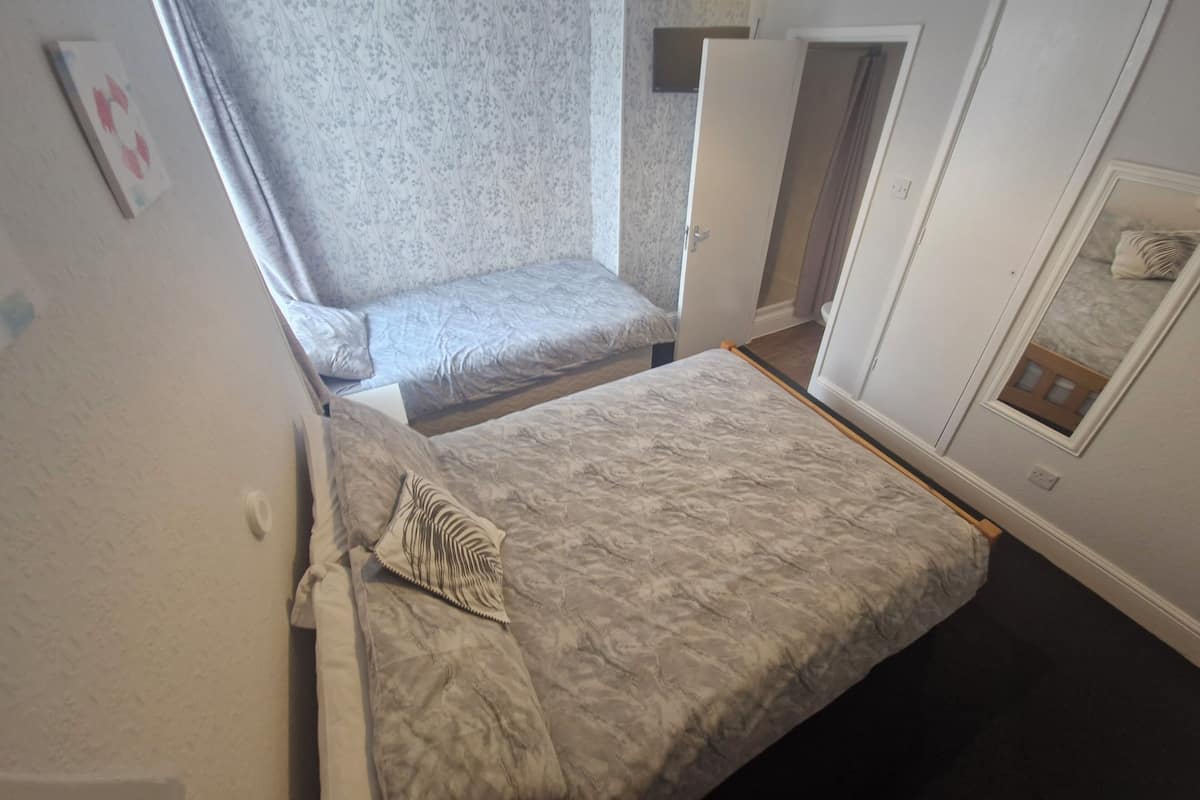Un dormitorio con dos camas, una ventana con cortinas, una puerta y una lámpara de pared.