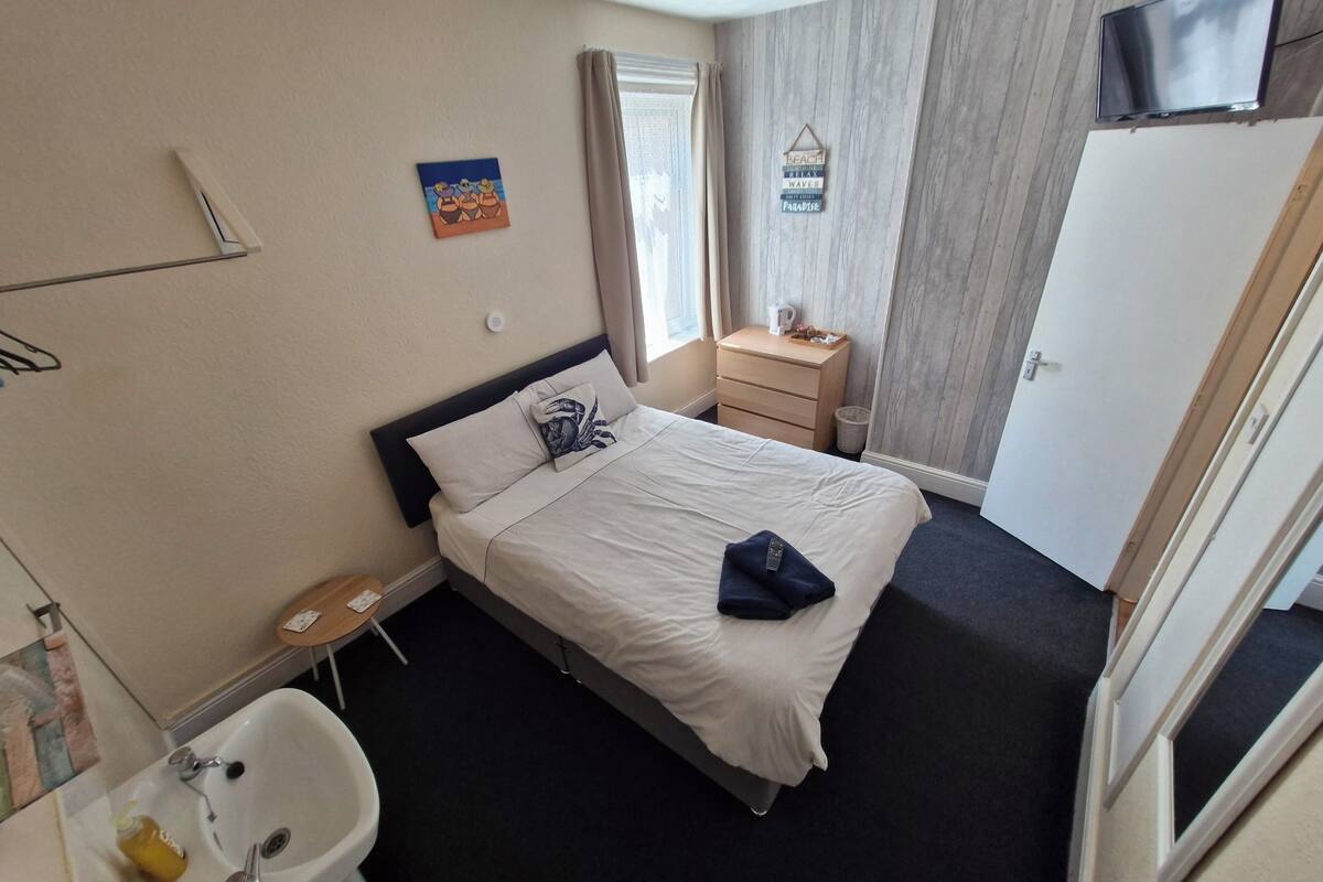 Habitación de hotel con cama, mesita de noche, televisor, ventana con cortinas y una obra de arte colgada en la pared.