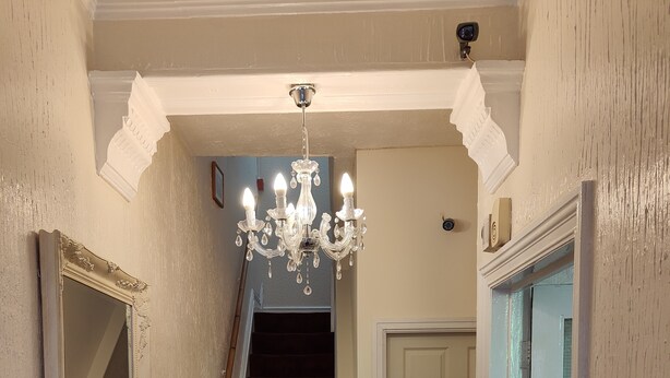 Un couloir orné d’un lustre, avec un escalier, une porte portant l’inscription « PRIVÉ » et une petite table sur laquelle sont posés divers objets.