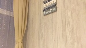 Un mur en bois sur lequel est accrochée une pancarte indiquant une liste de mots liés à la plage. Une bouilloire blanche et une télécommande sont posées sur une table en bois.