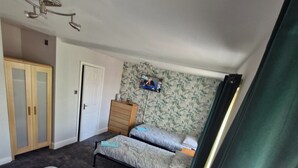 Une chambre avec deux lits, une armoire, une commode et un téléviseur fixé au mur.