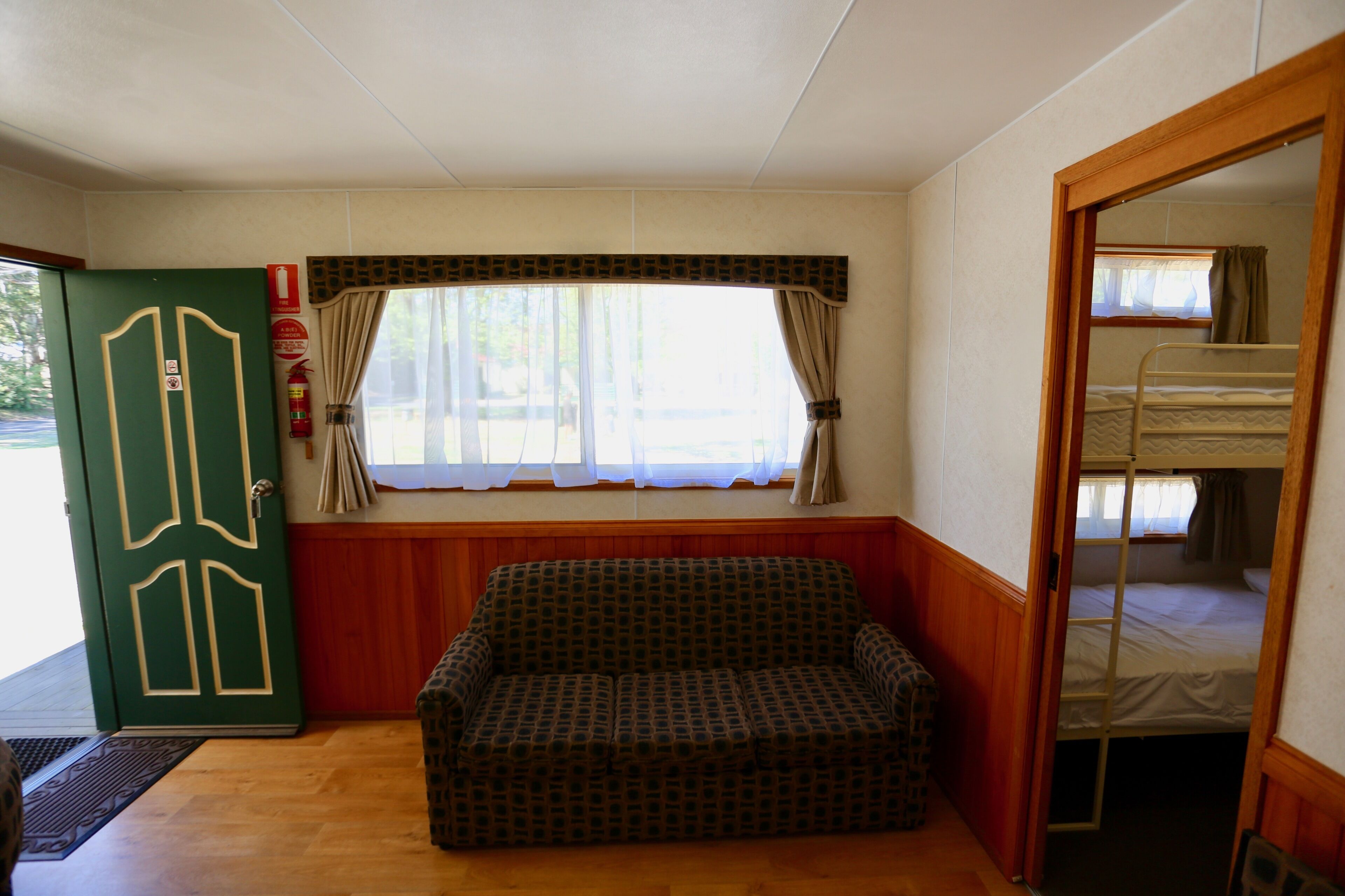 Quarto com porta verde, janela com cortinas, beliche e sofá estampado.