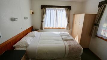A hotel room with a bed, a wardrobe, a window with curtains, and a bedside table.
