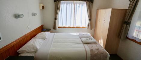 Quarto de hotel com cama, guarda-roupa, janela com cortinas e mesa de cabeceira.