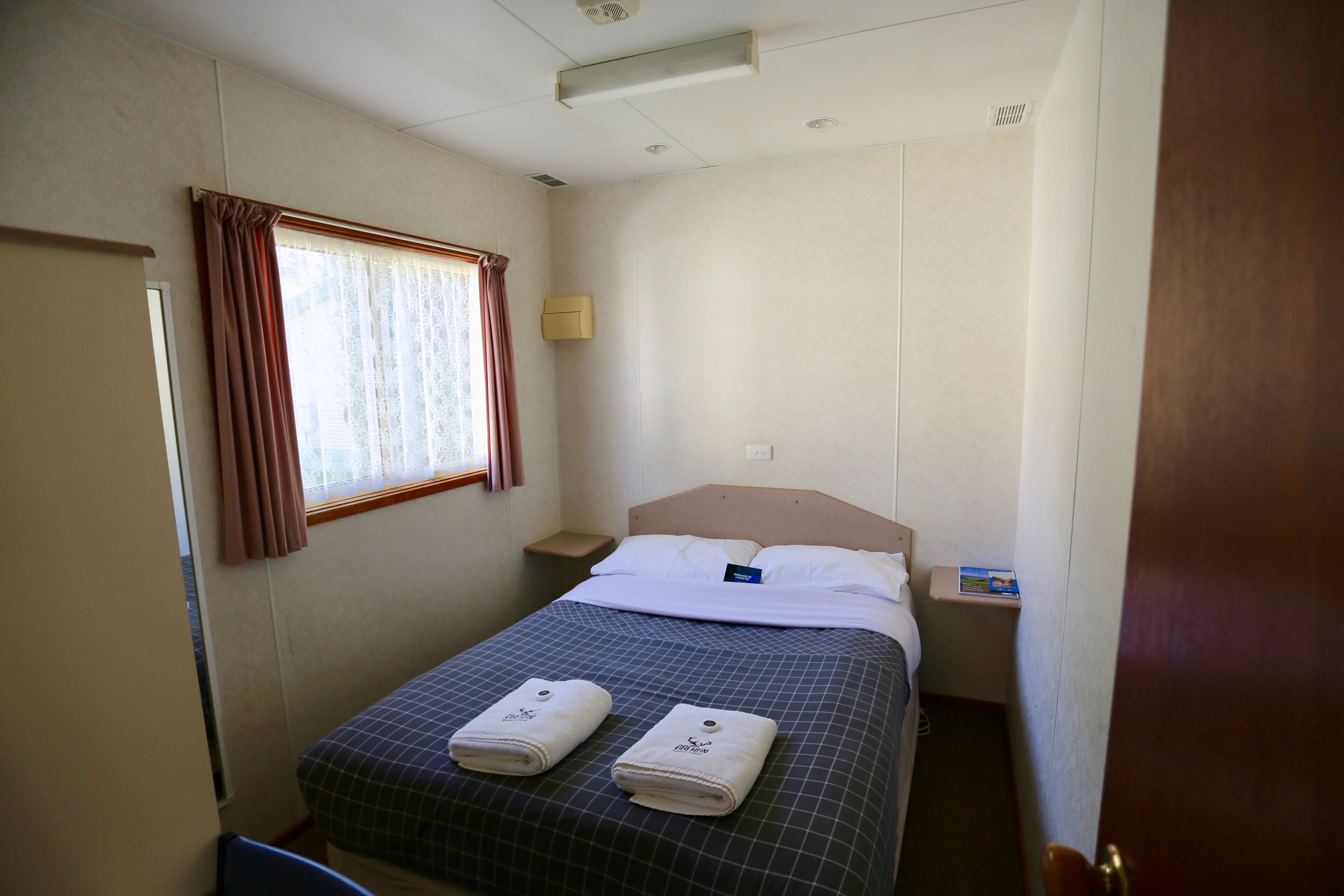 Una habitación de hotel pequeña y ordenada con una cama individual, una mesita de noche y una ventana con cortinas.
