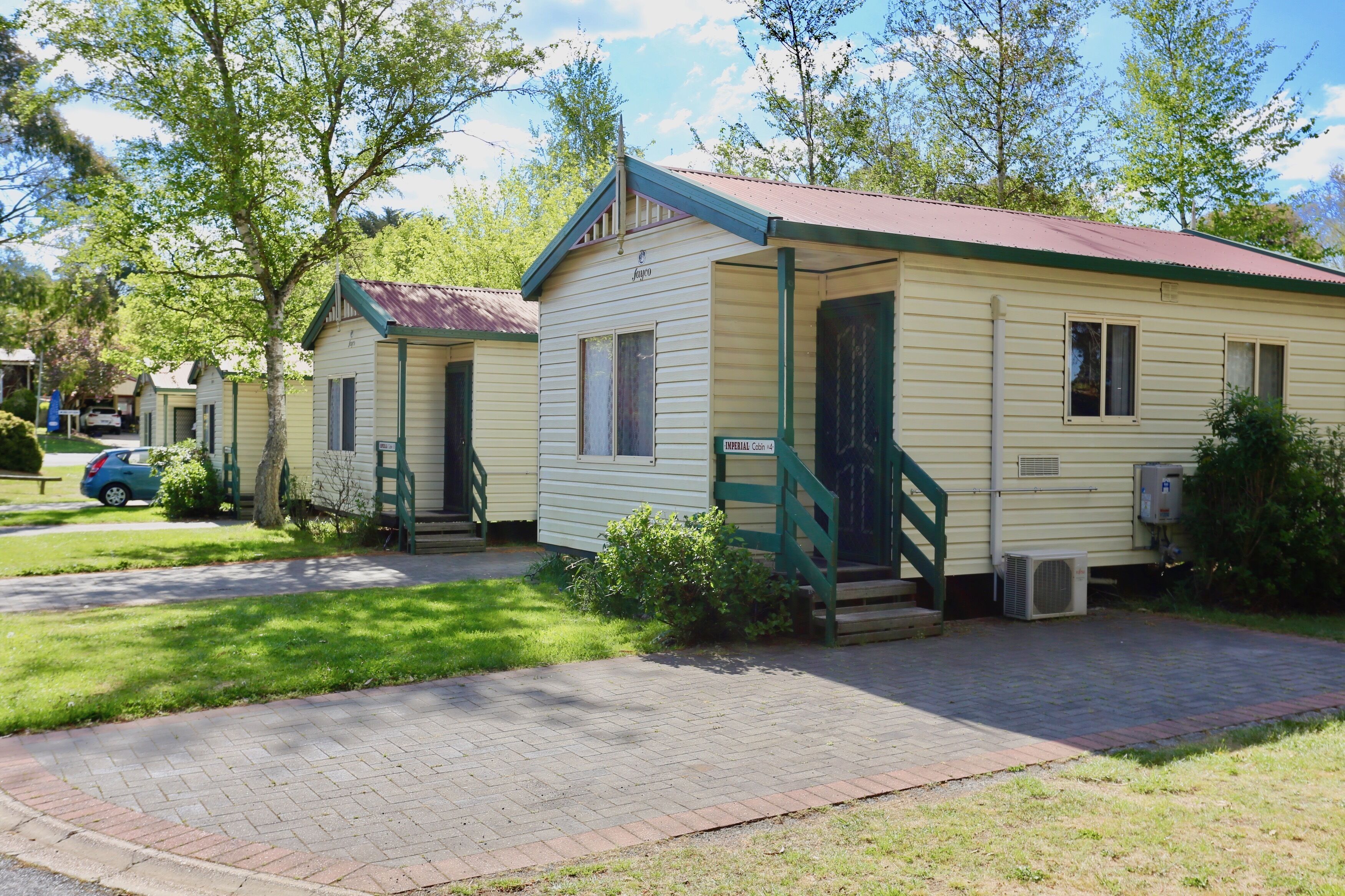 A row of small, single-story cabins with green trim and a red roof, each with a front porch and a small front yard.