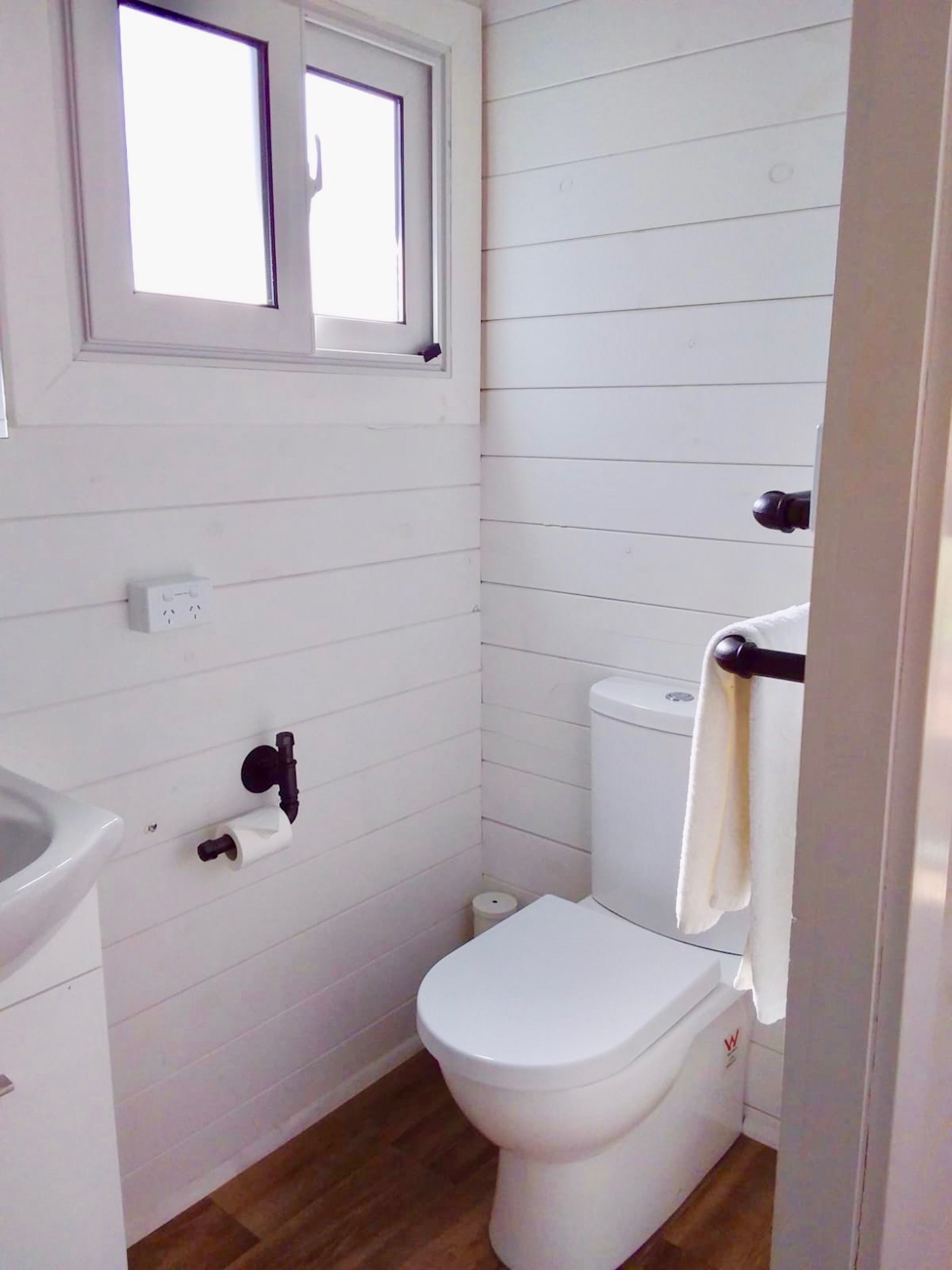 Ein kleines Badezimmer mit weißen Wänden, einer Toilette, einem Fenster und einem Handtuchhalter.